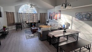 Een ruime woonkamer met een hoge plafond, een eettafel, een bank en een tafelvoetbaltafel.