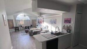 Een moderne keuken met een centraal eiland, een eetgedeelte met een ronde tafel, en een woonkamer met een bank en een plafondventilator.