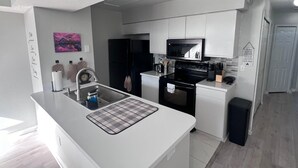 Een moderne keuken met witte kasten, een zwarte koelkast, een magnetron en een roestvrijstalen spoelbak.