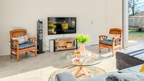Moderni olohuone, jossa on litteänäyttöinen televisio, puiset tuolit, lasinen sohvapöytä ja sohva.