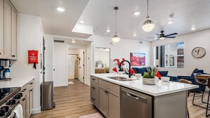Une cuisine moderne dotée d’un îlot central, d’appareils électroménagers en acier inoxydable et d’un coin repas avec un canapé bleu et une horloge au mur.