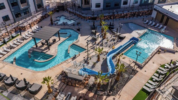 Un espace piscine à plusieurs niveaux, agrémenté de divers éléments aquatiques, dont un toboggan, et entouré de chaises longues et de transats.