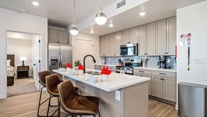 Une cuisine moderne dotée d’un îlot central, d’appareils électroménagers en acier inoxydable et d’un coin repas avec des chaises marron.