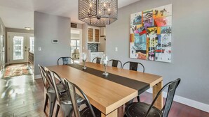 Un coin repas avec une table et des chaises en bois, un luminaire décoratif suspendu et un collage coloré accroché au mur.