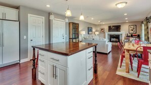 Une cuisine moderne avec des meubles blancs, un îlot central en bois, des luminaires suspendus et un coin repas avec des chaises rouges et une table en bois.