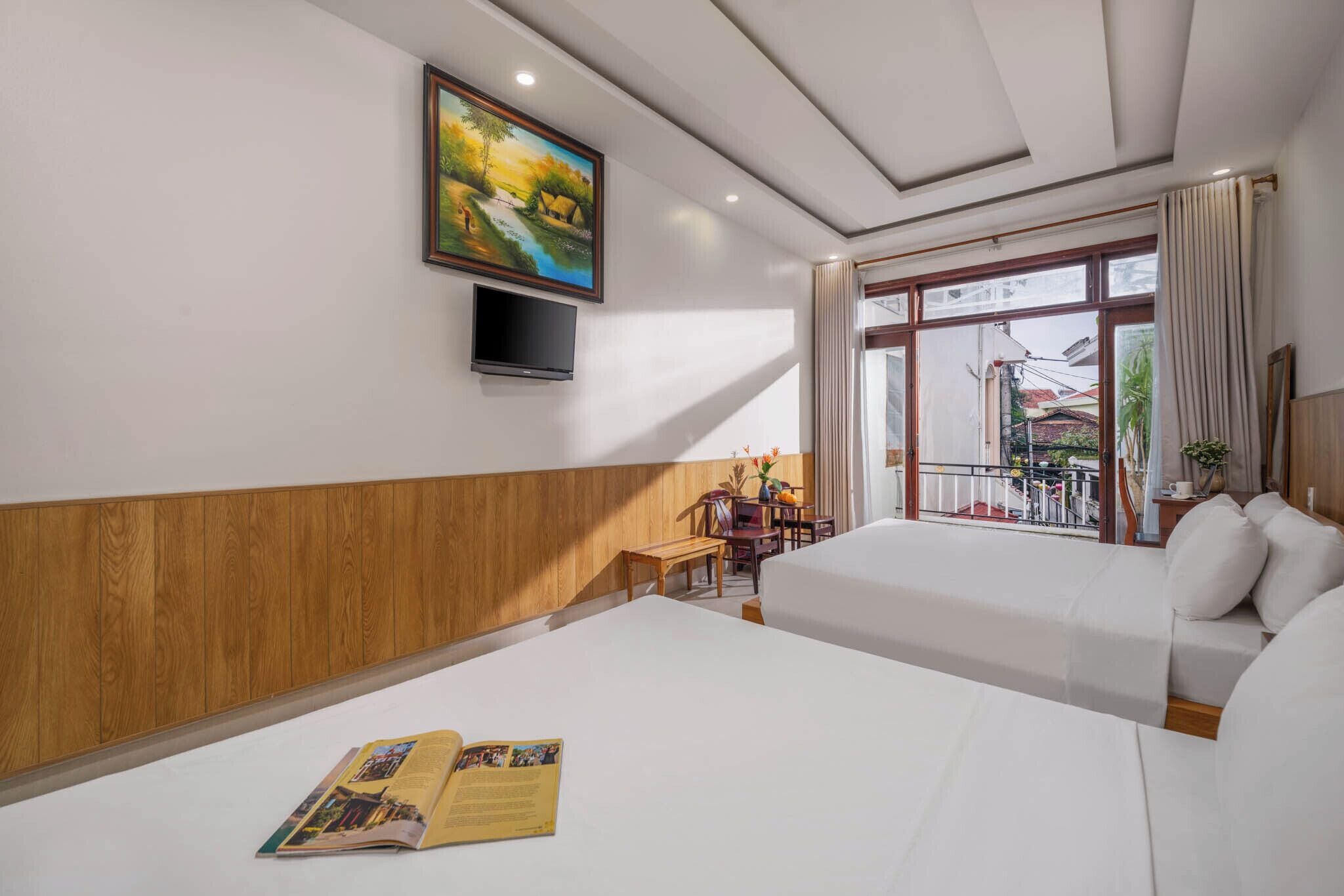 Quarto de hotel com duas camas, um quadro na parede, uma televisão e uma varanda com vista para o exterior.