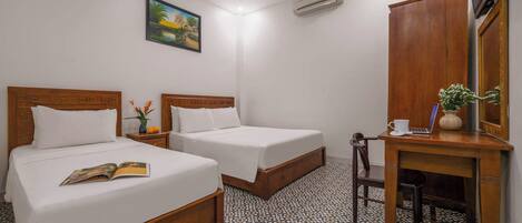A hotel room with two beds, a desk with a laptop, a mirror, and a painting on the wall.