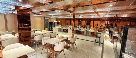 A modern restaurant with a bar area, seating arrangements, and a counter with various food items.