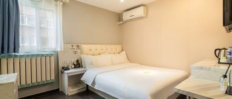 A hotel room with a bed, a bedside table, a nightstand, a window with curtains, a radiator, an air conditioner, and a television.