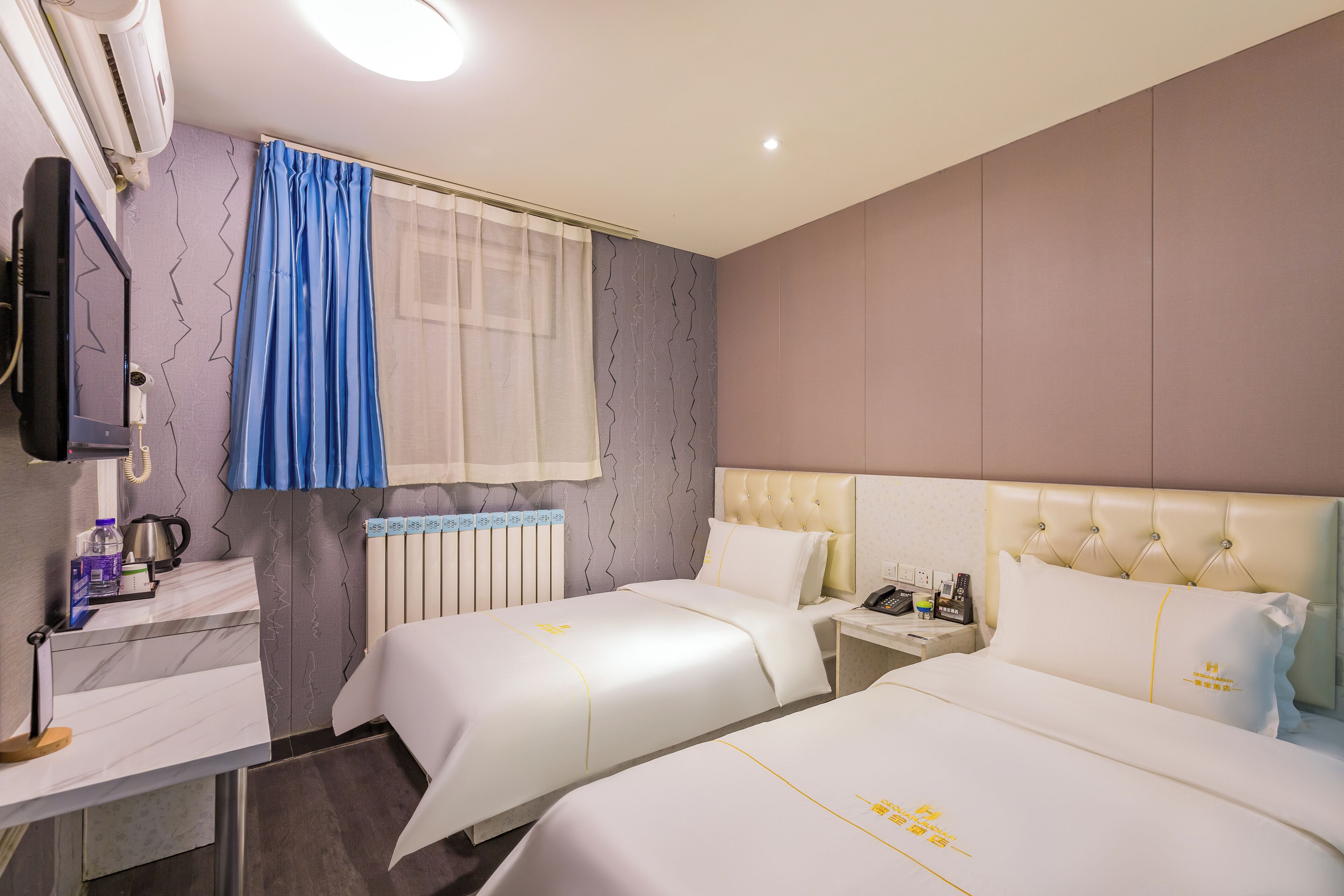 A hotel room with two beds, a desk, a TV, and a window with curtains.