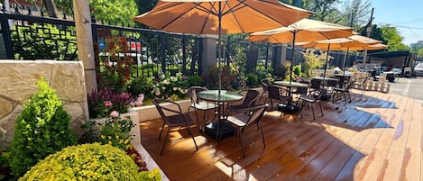 Un patio al aire libre con piso de madera, mesas redondas y sombrillas marrones.