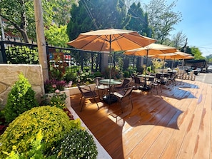An outdoor patio with wooden flooring, round tables, and brown umbrellas. - Dexin Xinyue Hotel (Beijing)