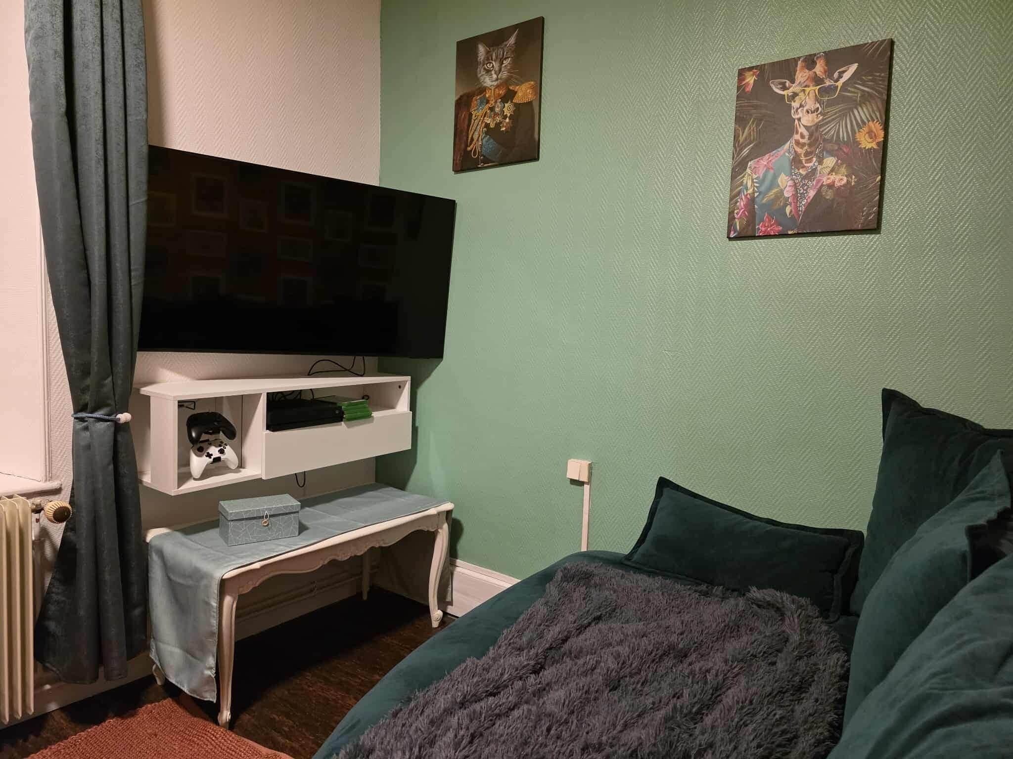 Un dormitorio con cama, televisor sobre un mueble bajo, una mesita y una obra de arte en la pared.
