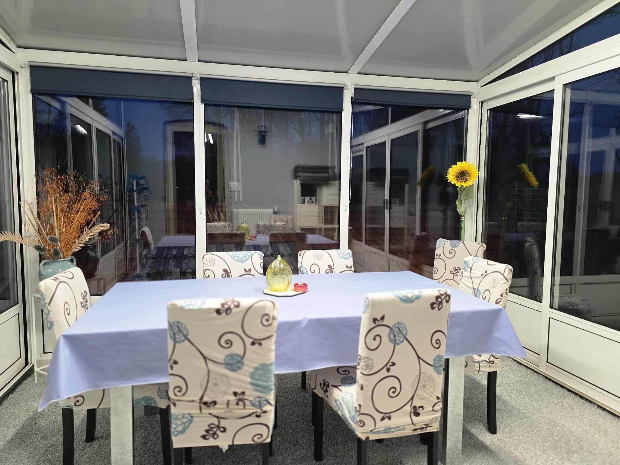 Un invernadero con una mesa y sillas, ventanas amplias y un jarrón con plantas secas.