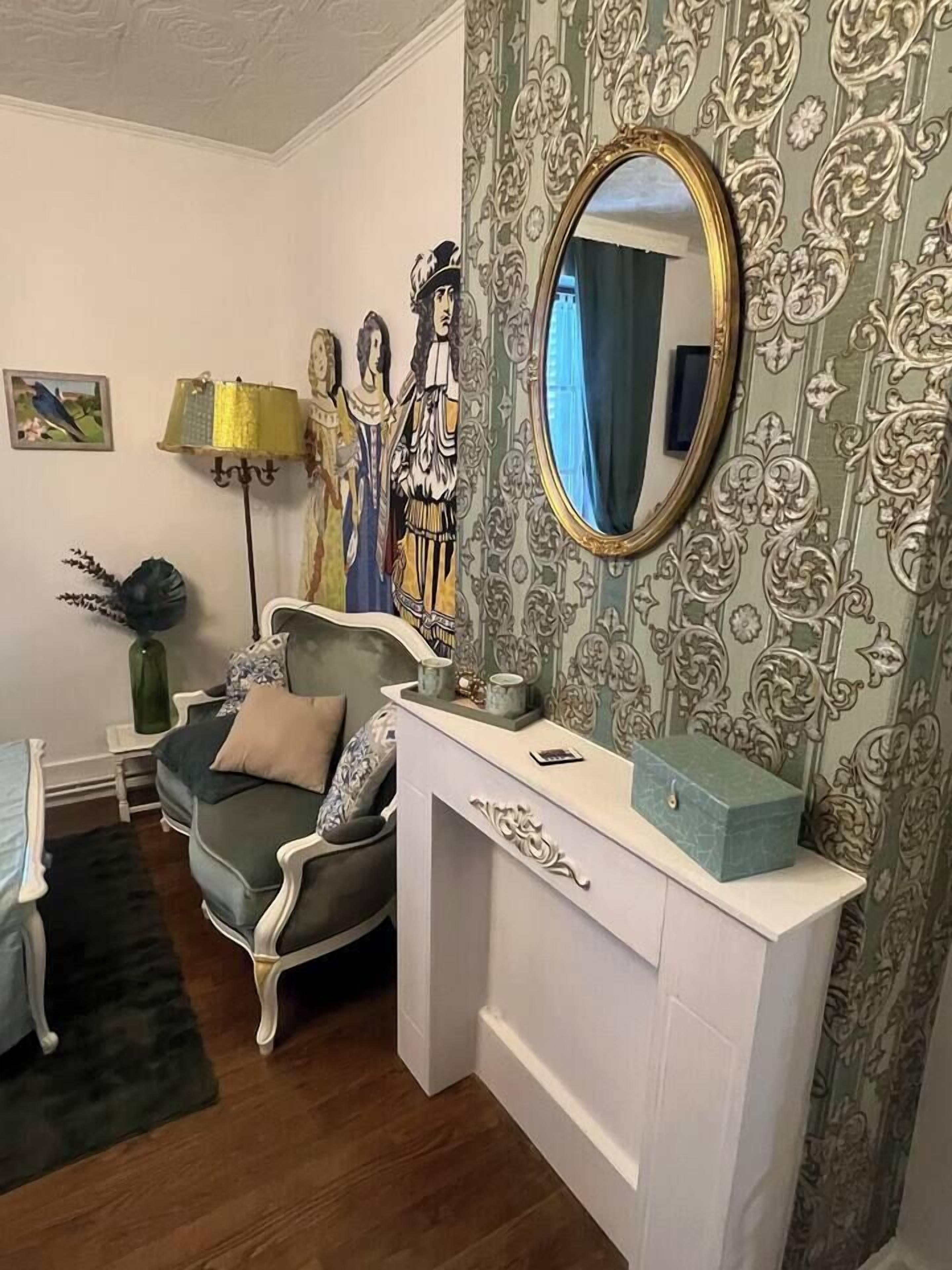 Una habitación con un sofá gris, una consola blanca con espejo y un papel tapiz estampado.
