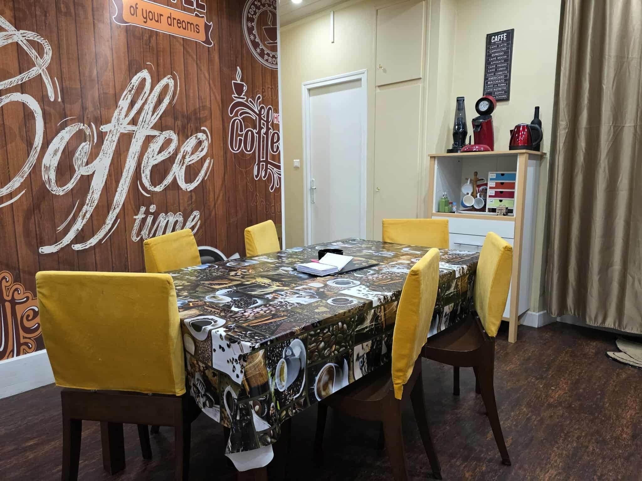 A dining area with a coffee-themed tablecloth, yellow chairs, and a menu board.