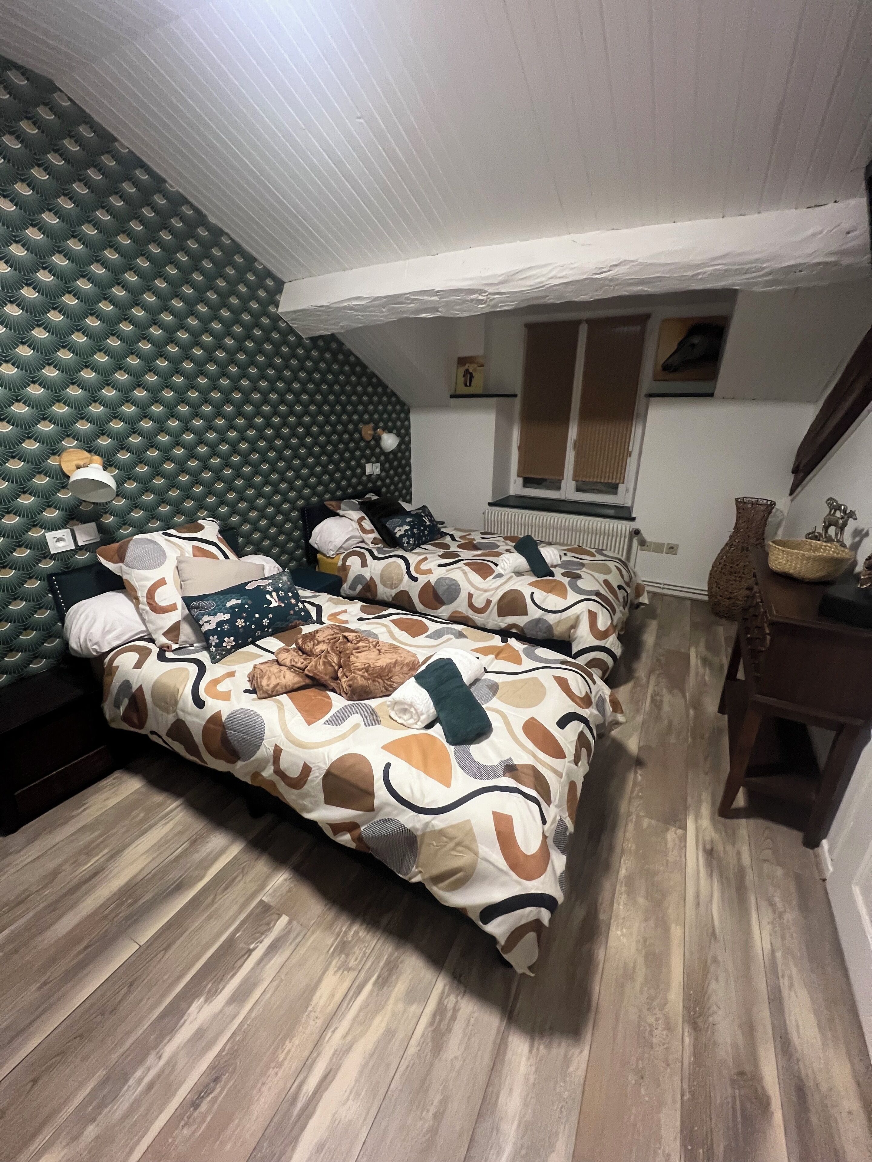 A room with two beds, a radiator, a wooden floor, and a green acoustic panel on the wall.