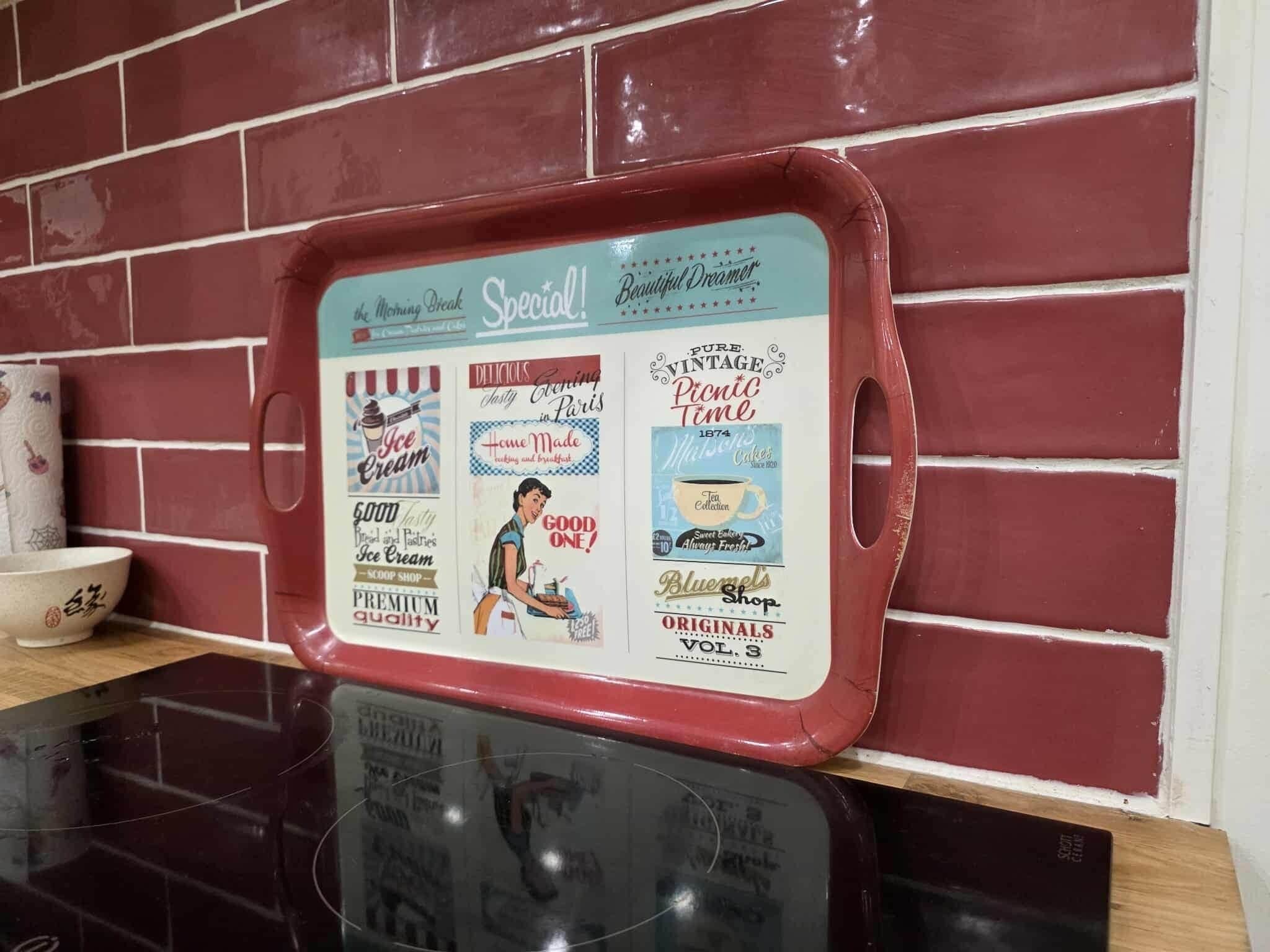 Un plateau de style rétro, orné de diverses publicités anciennes, est posé sur un plan de travail de cuisine, le tout adossé à un mur de briques.