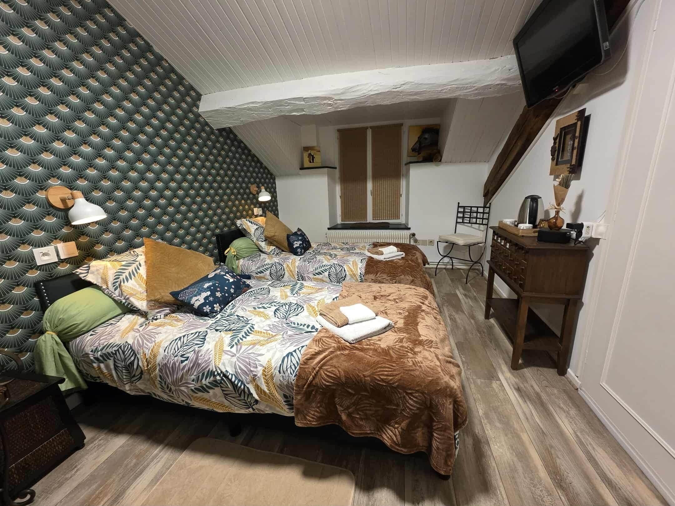 A cozy bedroom with a patterned headboard, a bed with multiple pillows, a desk with a chair, and a television mounted on the wall.