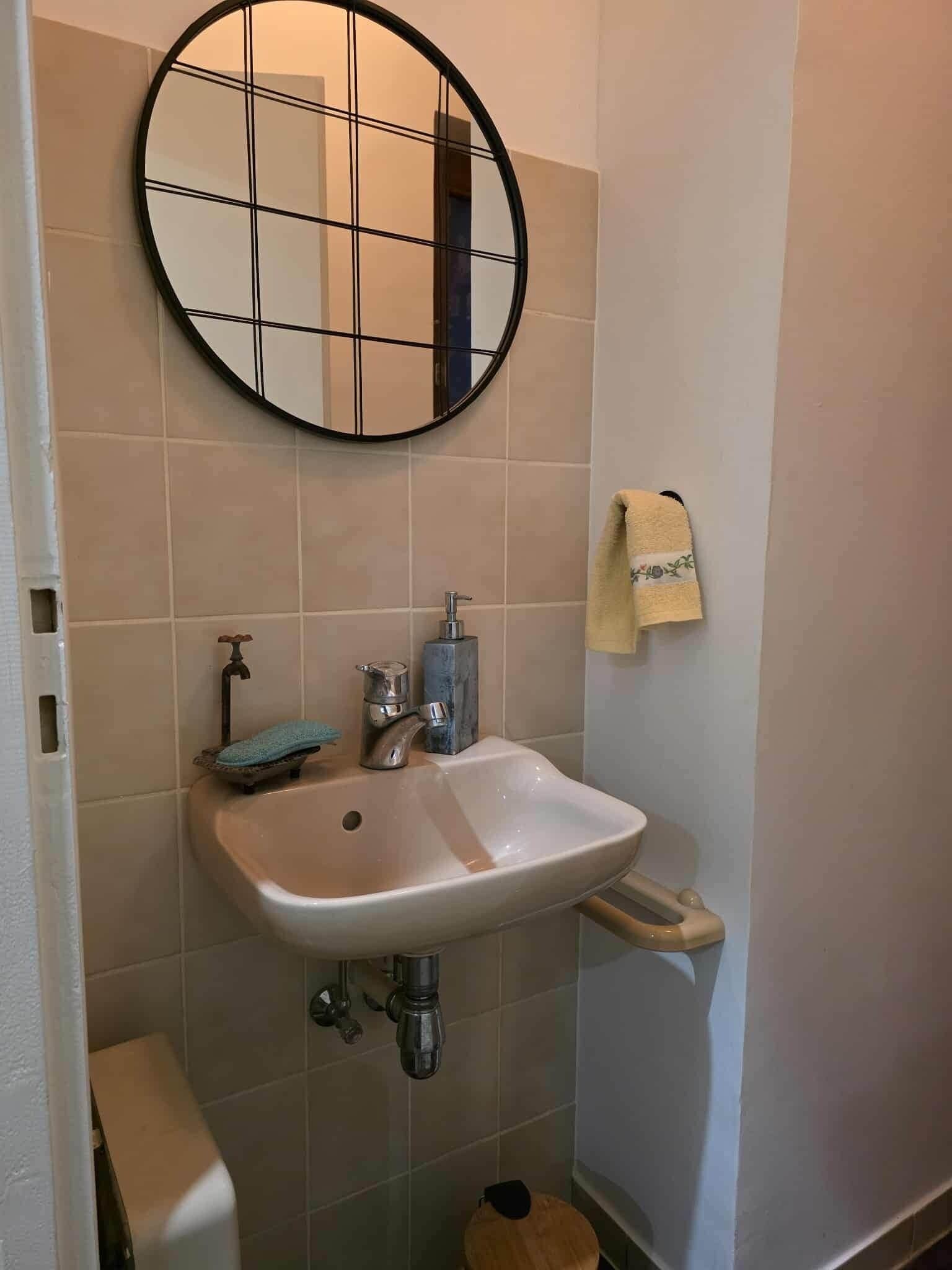 A bathroom with a white sink, a round mirror with a black frame, and a towel hanging on the wall.