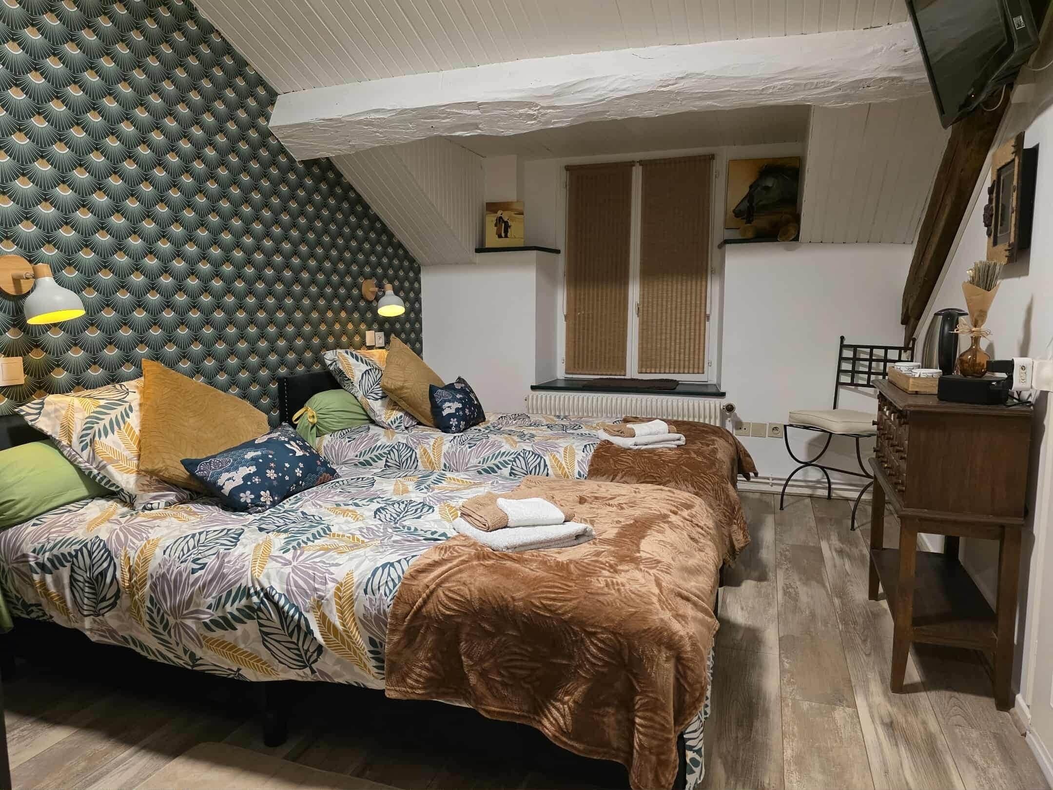 Makuuhuoneessa on kuviollinen sängynpääty, useilla tyynyillä varustettu sänky, puinen työpöytä ja ikkuna, jossa on sälekaihtimet.