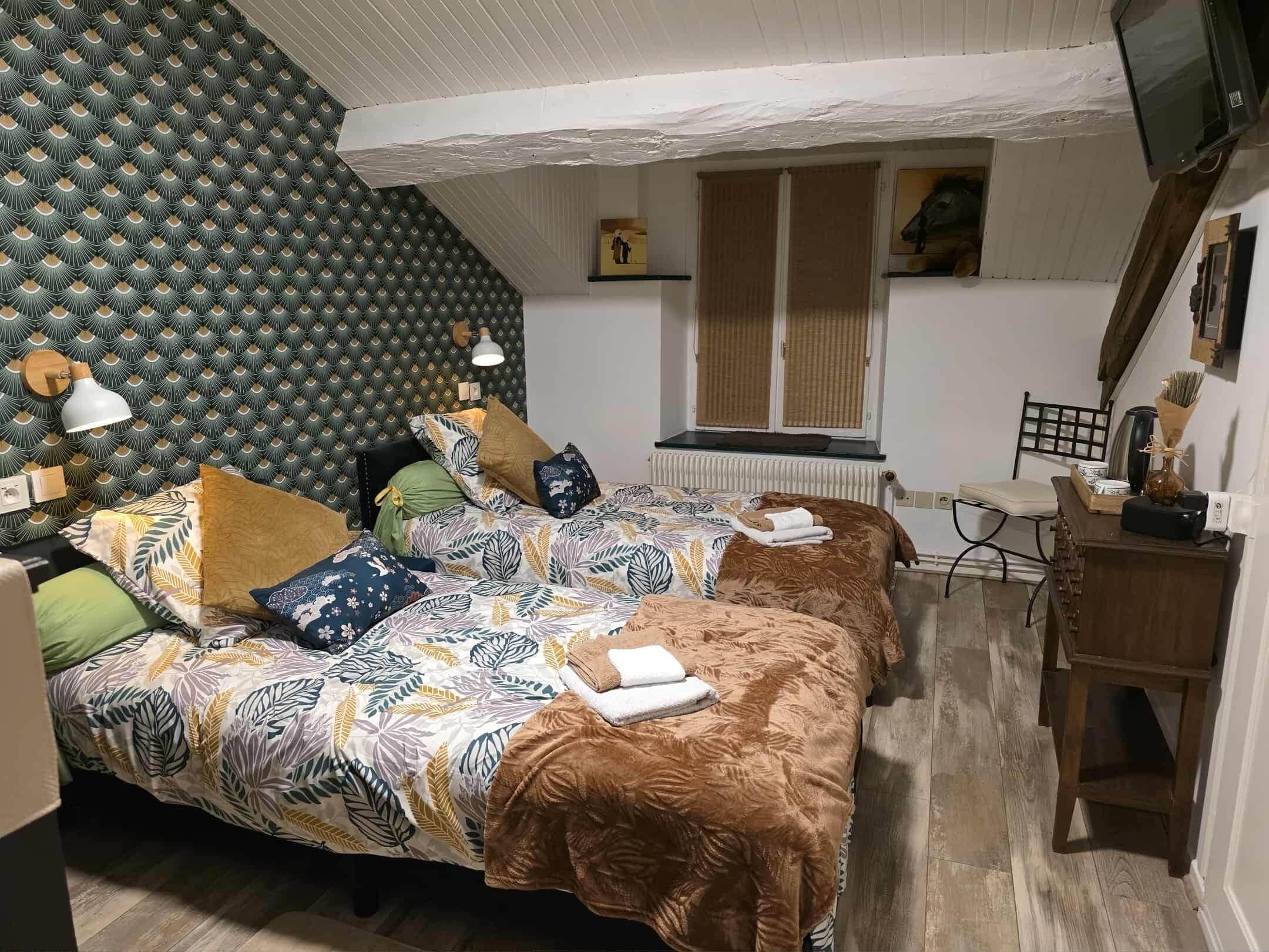Une chambre avec deux lits, un papier peint à motifs, un radiateur, une fenêtre avec des stores, un bureau en bois et une chaise.