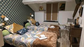 Une chambre avec deux lits, un papier peint à motifs, un radiateur, une fenêtre avec des stores, un bureau en bois et une chaise.