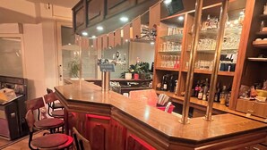 Una zona de bar con mostrador de madera, taburetes y estantes con copas y botellas.