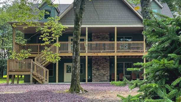 Une maison à deux étages, avec des fondations en pierre, une terrasse en bois et un escalier menant à l’étage supérieur.