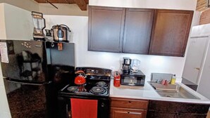 A compact kitchen with a black stove, a red kettle, a coffee maker, and a microwave. - Detroit Riverview Loft (Detroit)