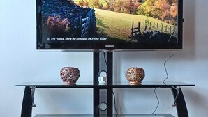 A television on a black stand with a scenic landscape wallpaper, two woven baskets, and a cable management box. - Detroit Riverview Loft (Detroit)
