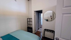 A bedroom with a bed, a bedside table, a mirror, and a door leading to another room. - Detroit Riverview Loft (Detroit)
