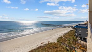 A beach with a pier extending into the ocean, a sandy beach, and a building with balconies overlooking the beach. - #2 Dreamscapes Oceanfront Oasis, Sea Pointe 605 (North Myrtle Beach)