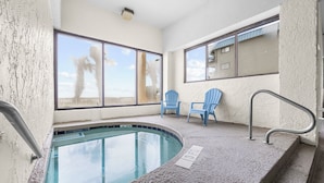 An indoor swimming pool with clear views of palm trees and a building through large windows.