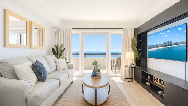 A modern living room with a sofa, coffee table, TV, and a balcony with a view of the sea. - #2 Dreamscapes Oceanfront Oasis, Sea Pointe 605 (North Myrtle Beach)