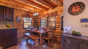 A rustic wooden cabin interior with a wooden dining table set for two, a bench, and a clock on the wall.