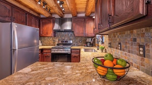 A kitchen with wooden cabinets, granite countertops, a stainless steel refrigerator, a stove, and a fruit bowl.