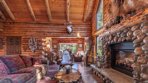A log cabin interior with a stone fireplace, a mounted deer head, and a cozy seating area.
