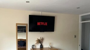 Un dormitorio con un aparador de madera, un espejo y un televisor en la pared mostrando 'NETFLIX'.
