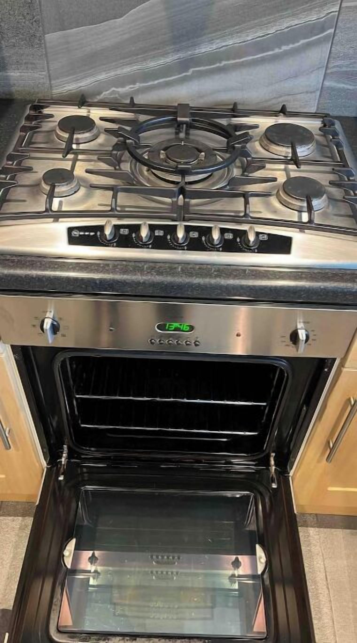 A kitchen with a stainless steel stove, oven, and a digital clock displaying 13:46.