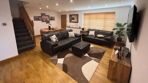 Un salón amplio con un sofá de cuero negro, una mesa de centro de madera y una zona de comedor con mesa y sillas de madera.
