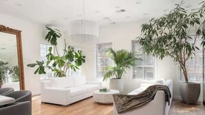 A spacious living room with white sofas, a coffee table, and large potted plants.