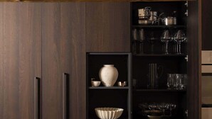 A modern kitchen with dark wood cabinets, a central island with a bowl of fruit, and a gas stove.