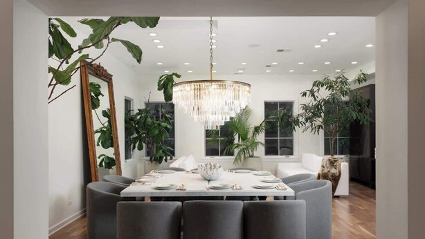 A modern dining area with a chandelier, round table, and grey upholstered chairs.