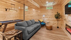 A cozy room with a pool table, a gray sofa, a blue chair, a small table with a board game, and a fireplace. - "Ultimate Luxe Escape with Private Movie Theater and Game Room" (Nelsonville)