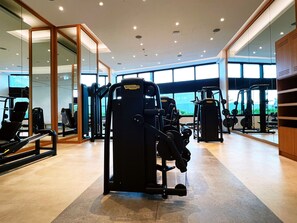 A modern gym with various exercise machines, large windows, and a clean, spacious layout.
