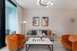 Een moderne woonkamer met een bank, twee oranje fauteuils, een salontafel en abstracte kunst aan de wand.