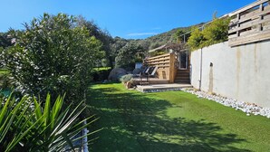 A modern outdoor area with a wooden deck, a concrete wall, and a well-maintained lawn. - Mini villa T3 air-conditioned, sea view, cosy & modern (Olmeto)