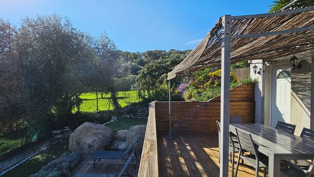 A wooden deck with outdoor furniture, a pergola, and a view of a green landscape with trees and a hill in the background. - Mini villa T3 air-conditioned, sea view, cosy & modern (Olmeto)