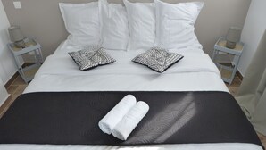 A neatly made bed with white and patterned pillows, a black bedspread, and two rolled towels. - Mini villa T3 air-conditioned, sea view, cosy & modern (Olmeto)